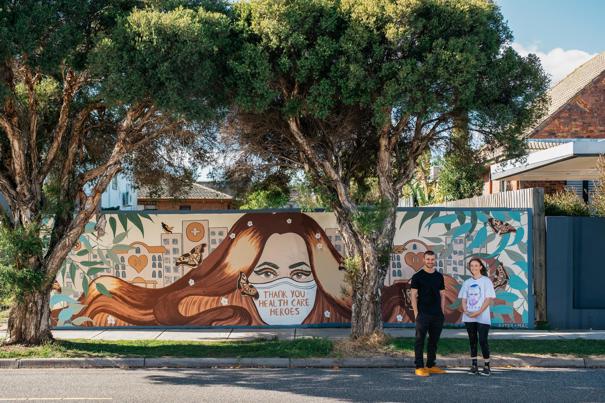Artists in front of a mural painted on a fence