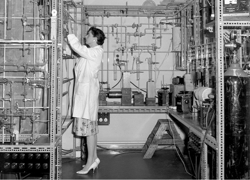 A woman standing in a laboratory, surrounded by equipment 