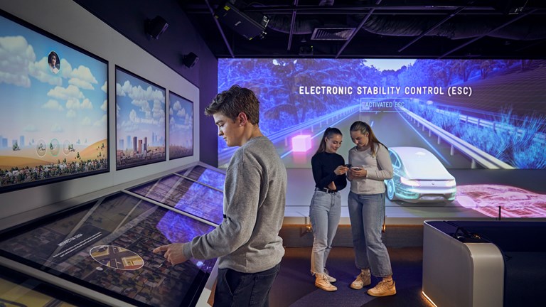 A student uses interactive touch screens in Road to Zero, whilst two other students refer to their mobile phone-guided app.