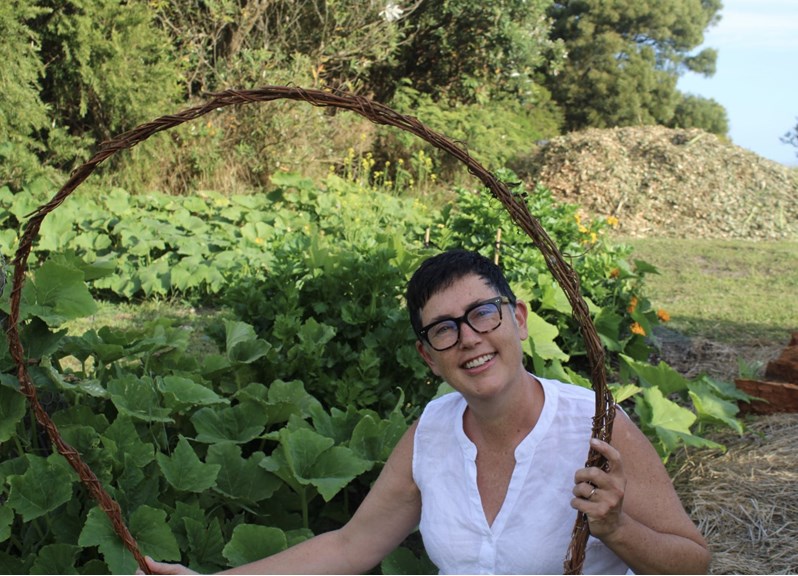 Woman holding a woven ring in front of a vegetable garden