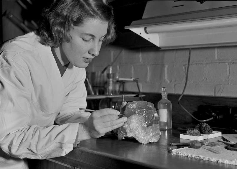 a woman in a lab coat leans over a large crystal
