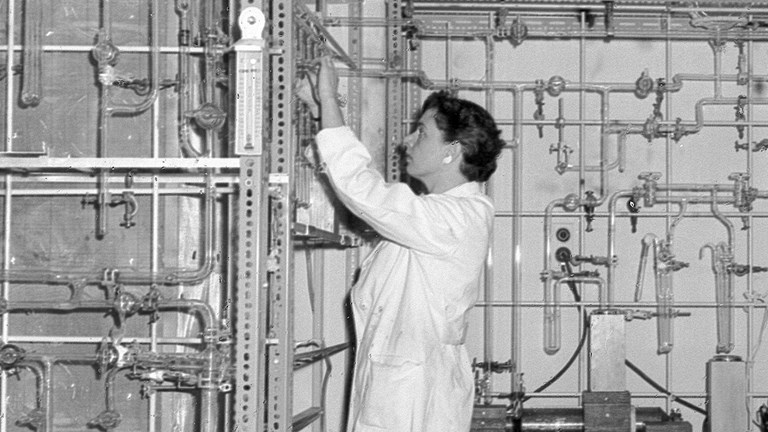 Black and white image of a woman wearing a lab coat in a science lab
