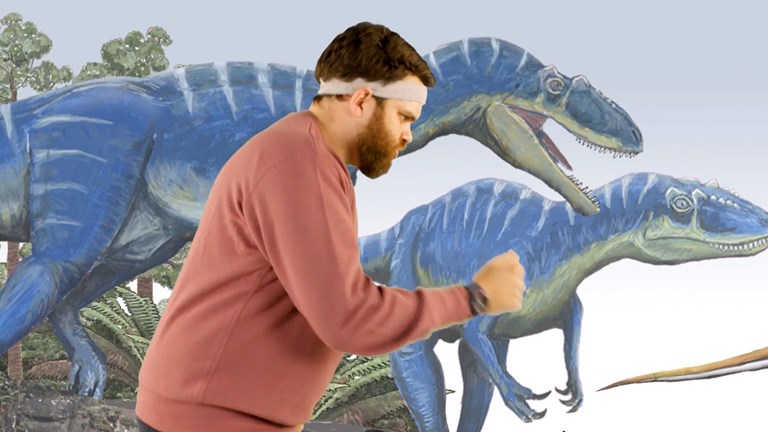 Man posing like a dinosaur in front of a dinosaur mural