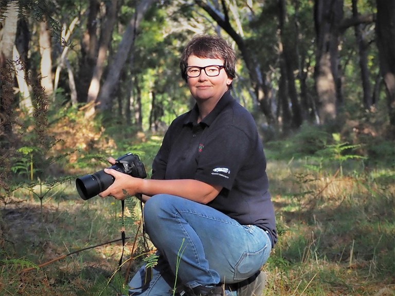 a woman kneeling in bushland holding a camera