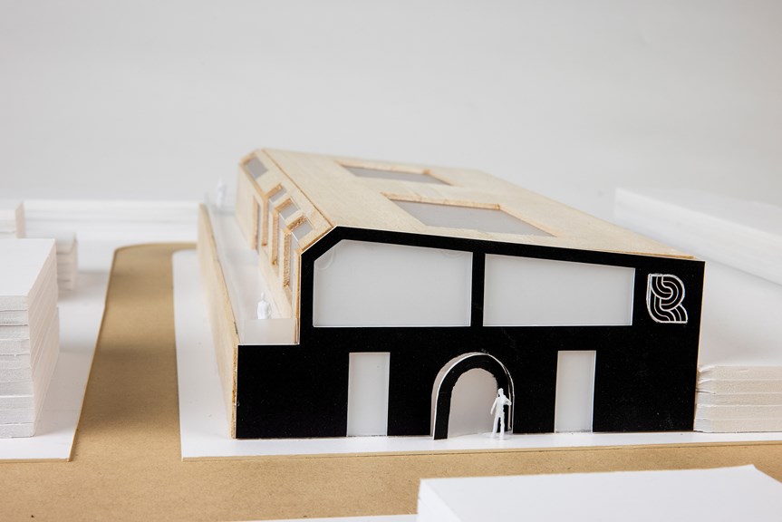A close up of an architectural model with the Track Records logo. The building is two story’s high with a black front façade, a balcony along one side and two large windows in the roof.