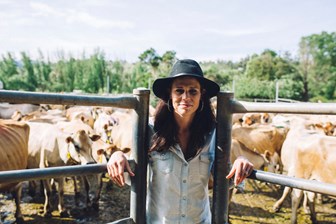 Woman wearing a black hat standing between two open gates, several cows can be seen gathered behind her