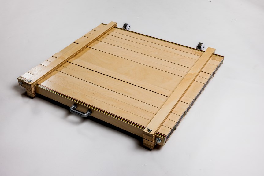 The image shows the portable animation table lying down. It is made of wood, and its wheels and handle are visible in the shot. It resembles a suitcase.