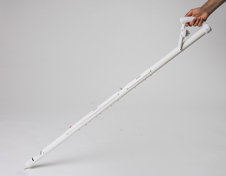 An image of a white cane made from plastic tubing. It is being held up by a hand. The cane has a switch in the middle and a sensor towards the base.