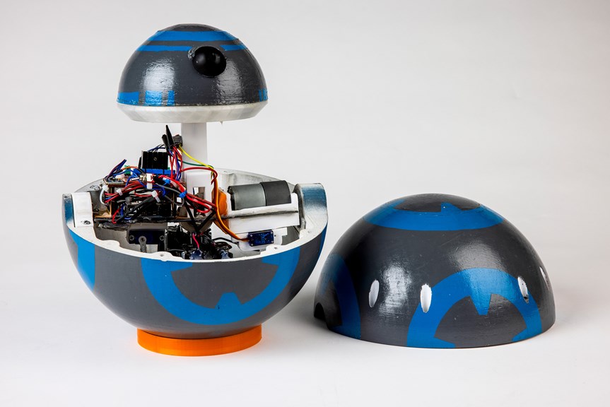 An image of a robot painted grey with a blue spherical design. The top half of the casing has been taken off to show the internal counterweight.