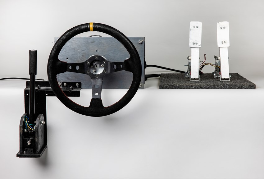An image of a racing simulator prototype. A gear box, steering wheel and pedals are displayed in a row.