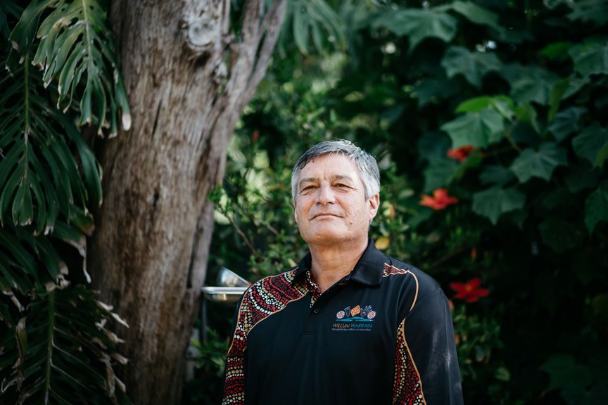 Man wearing a black t-shirt with an Aboriginal motif standing in a lush garden