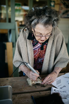 Woman using a tool to engrave possum skin