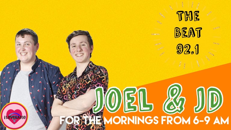 The image shows Joel and JD standing next to each other smiling, against a yellow and orange background. There is text reading “Joel & JD for the mornings from 6-9am”.