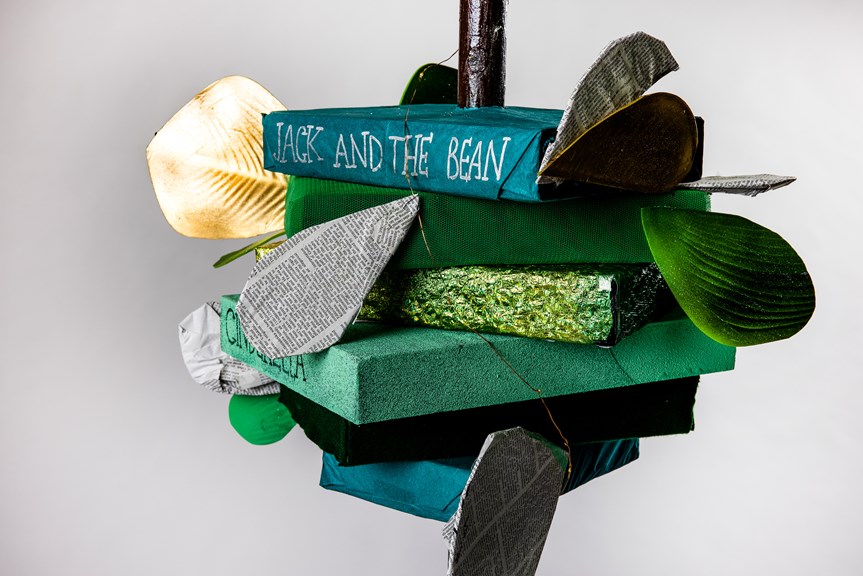A detail of a beanstalk made from stacked green books. One is titled ‘Jack and the Bean’. The set-piece is decorated with leaves made from book pages and green and gold material.