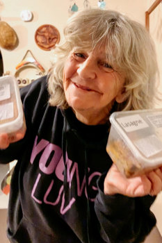 A woman is smiling and holding food containers