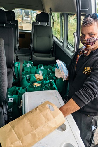 Man wearing a mask. He is standing at the door of van loaded with food deliveries.