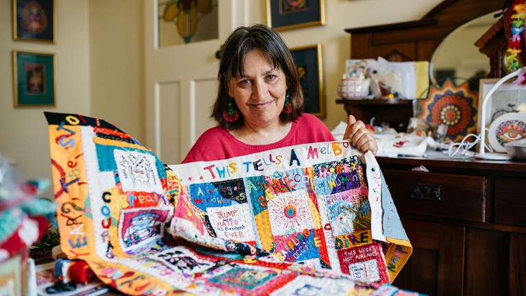 Woman posing holding an embroidered quilt