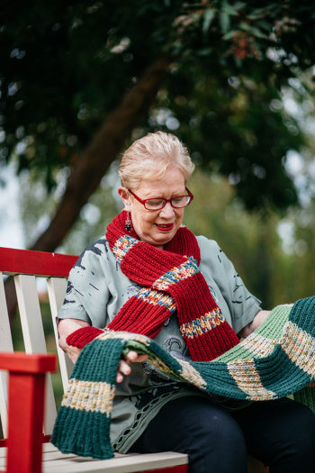 Woman sitting on a park bench she has a scarf around her neck and is also holding a scarf