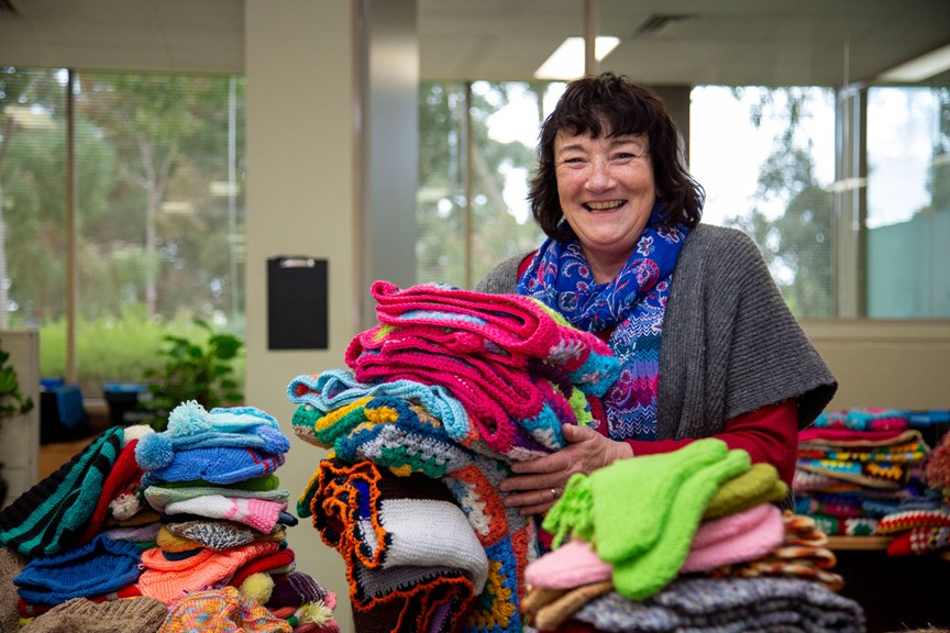 Woman standing with piles of knitting. She is smiling