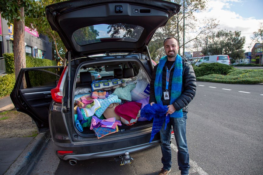 Man stand behind a car. The rear door is open and the car is loaded with knitting