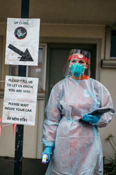 Woman standing outside a clinic wear PPE and holding a clipboard
