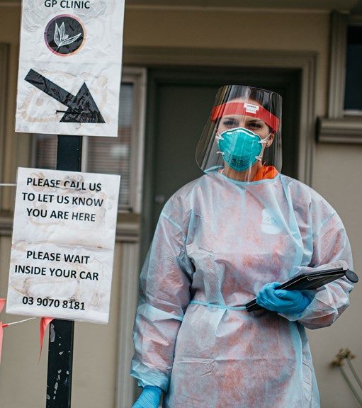Woman standing outside a clinic wear PPE and holding a clipboard