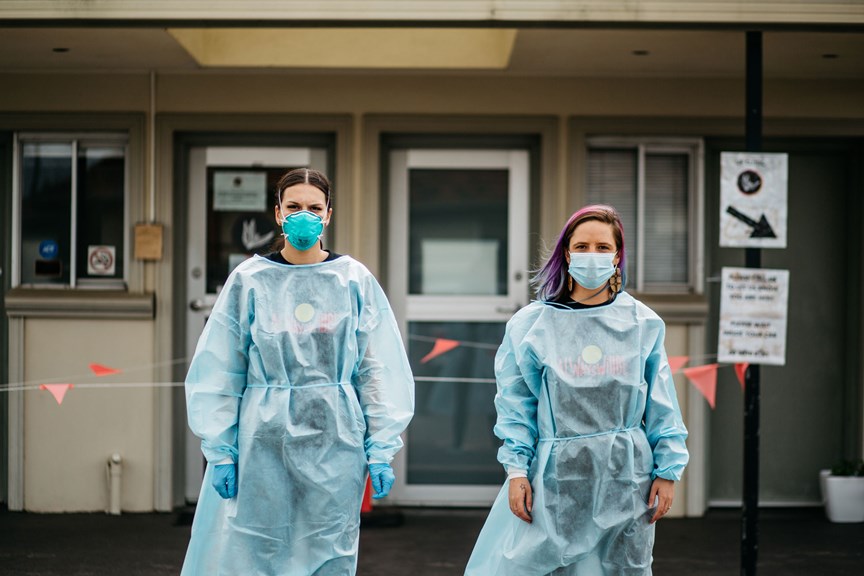 Two woman standing in front of a building wear PPE garmets