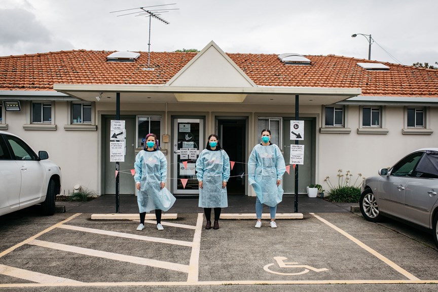 Three woman posing in front of a medical office wearing PPE garmets
