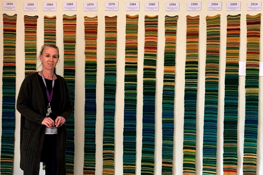 Woman standing front of an installation of narrow knitted strips