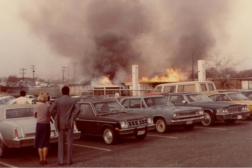 a photo of two people standing in a car park watching a building on fire 