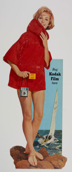 Poster featuring a woman wearing a red garment standing on rocks with an image of sailing boat behind her. Text "Buy Kodak film here"
