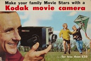 Cardboard poster advertising Kodak 8mm movie cameras, it features a man holding the a camera to his eye and two boys flying a kite.. The poster features the slogan 'Make your family Movie Stars with the Kodak movie camera...for less than £20'