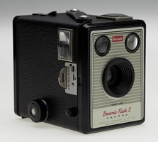Small box camera with fixed lens and two view finders. Camera body is black with its front face featuring grey stripes on silver with red and black text.
