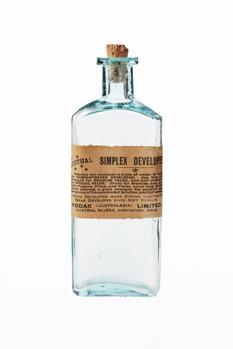 Glass bottle with cork stopper and paper label on the front with printed text in black ink. Bottle is empty of contents but there are some powdered residues on the cork.
