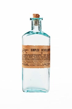 Glass bottle with cork stopper and paper label on the front with printed text in black ink. Bottle is empty of contents but there are some powdered residues on the cork.