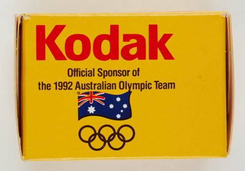 Side of a small yellow box. There text saying "Kodak: Official Sponsor of the 1992 Australian Olympic Team" The Olympic rings and Australian flag are also printed on it.