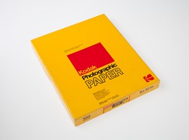 A yellow box with black and red text and a sticker of the same colours, printed with product details.