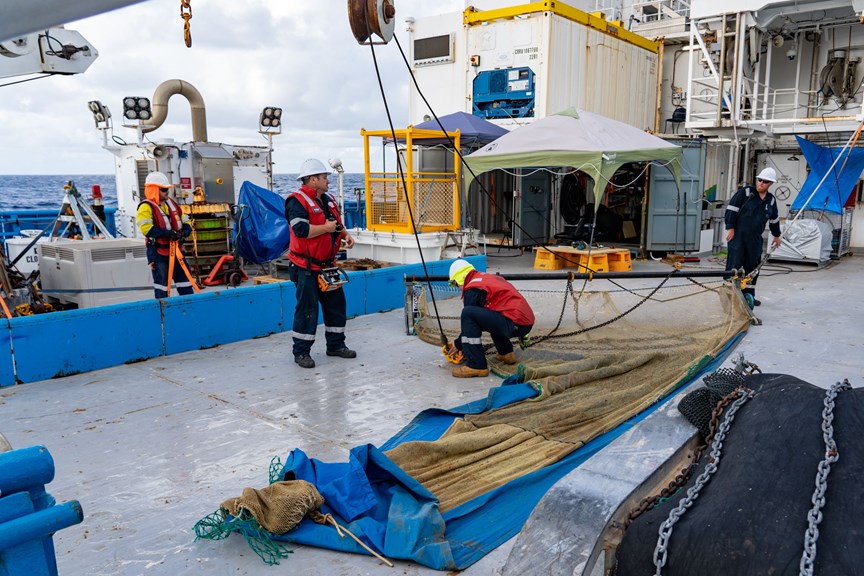 four men inspect a large net on the rear deck of a research ship