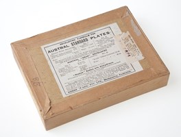 The back of a brown cardboard box printed developing formulae label. Box is sealed with brown paper.