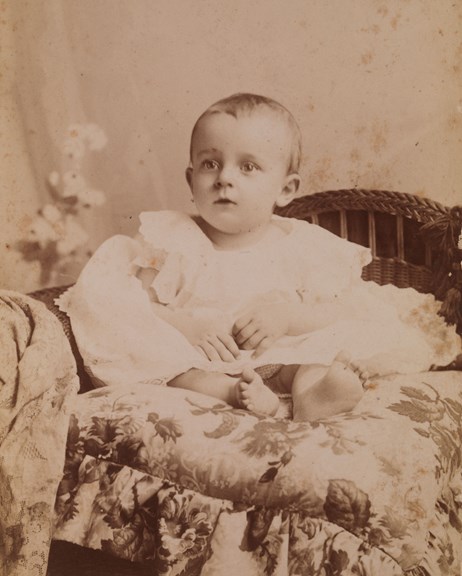 Portrait of a baby wearing a white robe sitting on a cushion