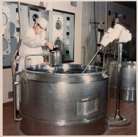 Man in white coat pouring liquid into stainless steel vat