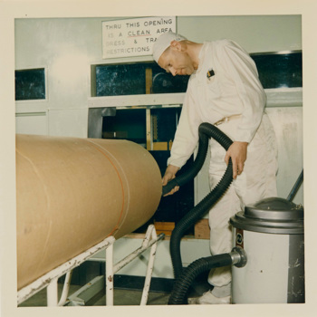 Man dressed in white overalls using an industrial vacuum cleaner