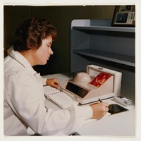 Woman sitting at a desk she is view a photograph and writing notes