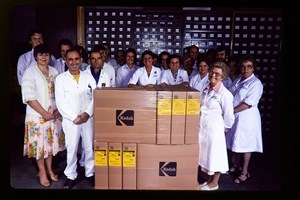 A group of men and woman standing next to a stack of cardboard boxes