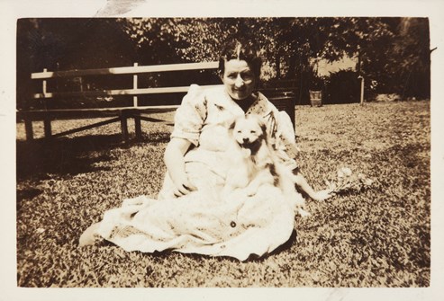 Woman seated on grass with small dog on lap.