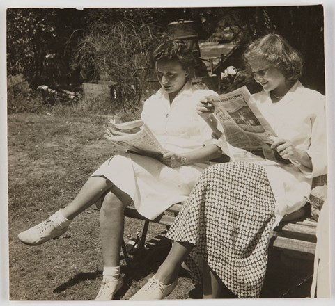 People sitting on bench with newspapers