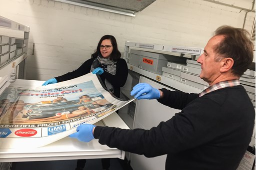 Man and woman placing a large poster into an open drawer with shelving behind them