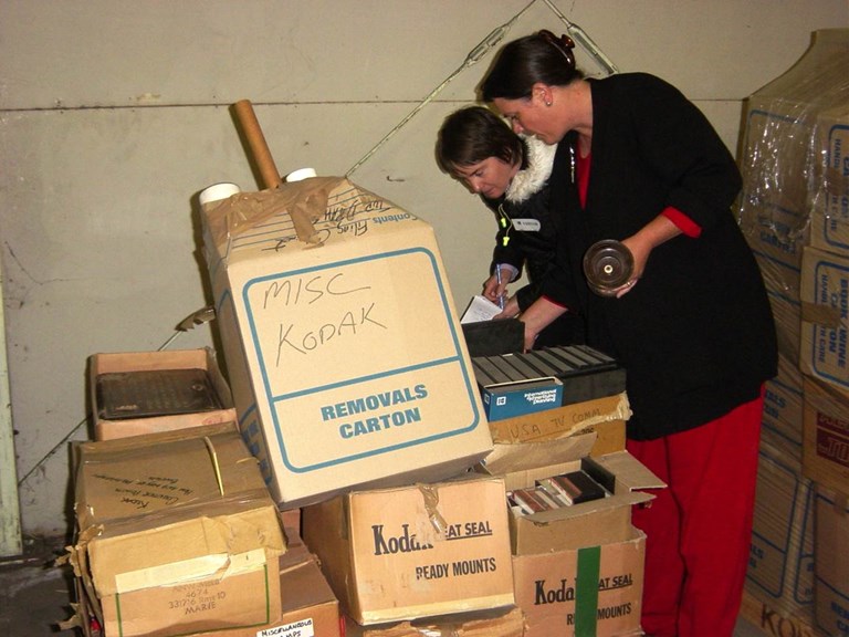 Two women sorting through boxes piled on top of each other