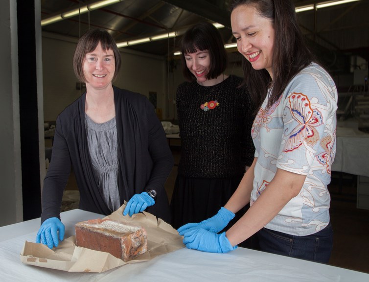 Museum conservator Noni Zachri, Kodak collection manager Hannah Perkins and curator Fiona Kinsey with unwrapped chimney brick from the Kodak Australasia Pty Ltd Coburg factory