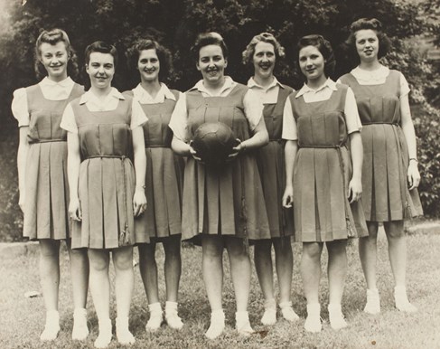 Seven women in sporting attire, one holding a basketball